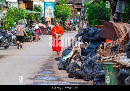 Un monaco visto camminare tra pile di rifiuti lungo la strada, gettato dai residenti dopo che le acque si sono ritirate. Dopo che la situazione delle inondazioni a Chiang mai si placò, i monaci di vari templi locali ripresero la loro elemosina, come al solito, in una città piena di rifiuti di oggetti danneggiati dalle inondazioni, fango e polvere dai sedimenti lasciati dietro dalle acque in ritirata. Sebbene le autorità governative e i residenti abbiano iniziato a pulire l'area e a rimuovere i detriti, molti punti sono ancora coperti di fango e polvere accumulati. Ci vorranno diverse settimane prima che la situazione torni alla normalità. Foto Stock