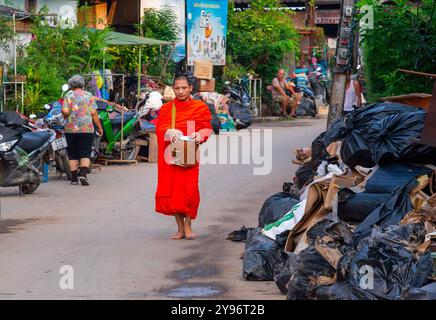 Un monaco visto camminare tra pile di rifiuti lungo la strada, gettato dai residenti dopo che le acque si sono ritirate. Dopo che la situazione delle inondazioni a Chiang mai si placò, i monaci di vari templi locali ripresero la loro elemosina, come al solito, in una città piena di rifiuti di oggetti danneggiati dalle inondazioni, fango e polvere dai sedimenti lasciati dietro dalle acque in ritirata. Sebbene le autorità governative e i residenti abbiano iniziato a pulire l'area e a rimuovere i detriti, molti punti sono ancora coperti di fango e polvere accumulati. Ci vorranno diverse settimane prima che la situazione torni alla normalità. Foto Stock