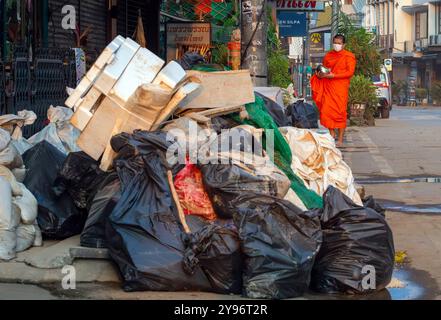 Un monaco visto camminare tra pile di rifiuti lungo la strada, gettato dai residenti dopo che le acque si sono ritirate. Dopo che la situazione delle inondazioni a Chiang mai si placò, i monaci di vari templi locali ripresero la loro elemosina, come al solito, in una città piena di rifiuti di oggetti danneggiati dalle inondazioni, fango e polvere dai sedimenti lasciati dietro dalle acque in ritirata. Sebbene le autorità governative e i residenti abbiano iniziato a pulire l'area e a rimuovere i detriti, molti punti sono ancora coperti di fango e polvere accumulati. Ci vorranno diverse settimane prima che la situazione torni alla normalità. Foto Stock