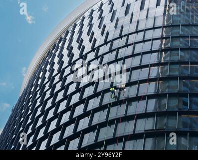 Persone non identificate che puliscono i finestrini di un edificio alto, i tecnici di accesso a fune offrono una soluzione di pulizia dei finestrini più sicura, veloce e conveniente. Foto Stock