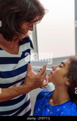 Nonna che somministra Saline Nasal Wash alla nipote per il trattamento dell'influenza. Gandmother ispanica che fa il lavaggio nasale per sua nipote da flushin Foto Stock