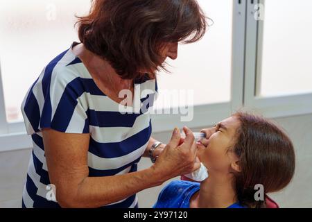 Nonna che somministra Saline Nasal Wash alla nipote per il trattamento dell'influenza. Gandmother ispanica che fa il lavaggio nasale per sua nipote da flushin Foto Stock