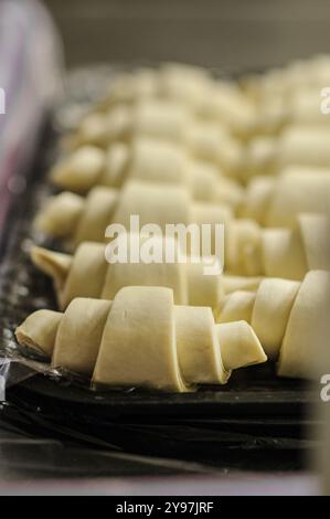 Croissant crudi disposti su una teglia da forno, pronti per il forno. Un assaggio della pasticceria professionale. Foto Stock