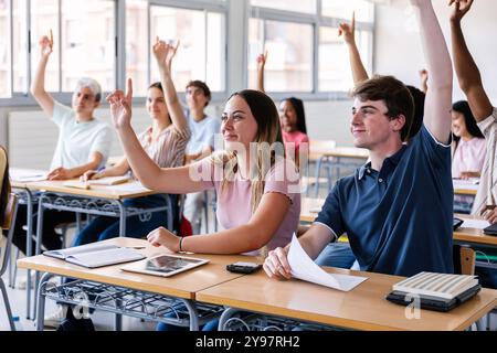 Gruppo di studenti delle scuole superiori che si alzano le mani in classe Foto Stock