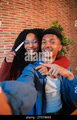 La coppia afroamericana verticale celebra un test di gravidanza positivo a casa. Abbracciate, sorridete, condividete l'eccitante notizia di aspettare un bambino, pieno di felicità, in attesa della loro nuova famiglia. Foto di alta qualità Foto Stock