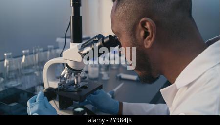 Laboratorio medico: Scienziato afroamericano analizza la struttura molecolare del vaccino o del farmaco sotto microscopio. Innovazioni nello sviluppo di vaccini contro nuovi virus. Microbiologia e medicina. Foto Stock