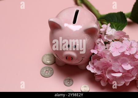 Salvadanaio rosa con monete e ortensie su sfondo rosa con spazio per il testo. Concetto di alfabetizzazione finanziaria. Foto Stock