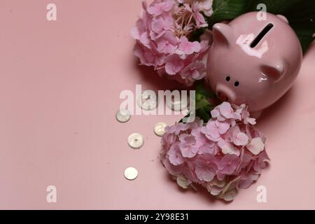 Salvadanaio rosa con monete e ortensie su sfondo rosa con spazio per il testo. Concetto di alfabetizzazione finanziaria. Foto Stock