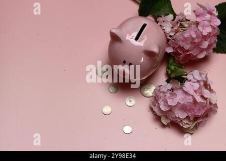 Salvadanaio rosa con monete e ortensie su sfondo rosa con spazio per il testo. Concetto di alfabetizzazione finanziaria. Foto Stock