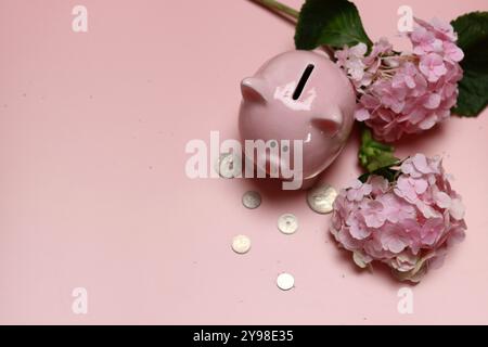 Salvadanaio rosa con monete e ortensie su sfondo rosa con spazio per il testo. Concetto di alfabetizzazione finanziaria. Foto Stock