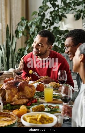 Un gruppo di amici condivide con gioia un pasto del Ringraziamento pieno di risate, cibo e calore. Foto Stock
