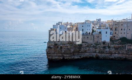 Le onde si infrangono dolcemente contro le antiche scogliere calcaree della Puglia, dove edifici imbiancati si aggrappano al bordo, mescolando natura e architettura sotto a. Foto Stock