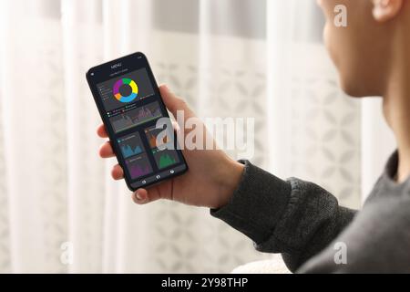 Uomo che monitora le letture dei contatori intelligenti sul telefono cellulare a casa, primo piano Foto Stock