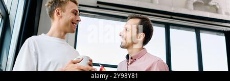 Due uomini affascinanti si godono una conversazione sentita, sorseggiando un drink in un ufficio caldo e invitante. Foto Stock