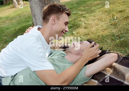 Una coppia felice condivide un momento tenero su una coperta, circondata da vegetazione lussureggiante in una giornata di sole. Foto Stock