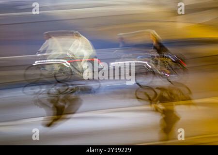 Panning dinamico per catturare i ciclisti con sfocature in movimento nelle strade della città di notte. Luci vibranti e movimento dinamico trasmettono una vita urbana frenetica. Foto Stock