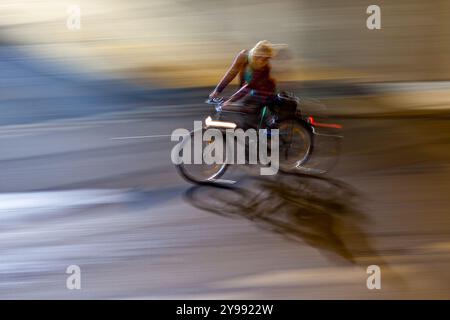 Una panoramica dinamica che cattura un ciclista che attraversa la città di notte, mostrando velocità e movimento in un ambiente urbano. Foto Stock