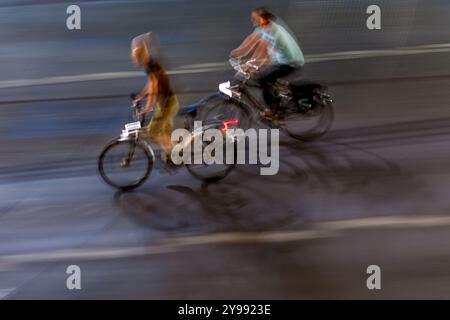 Panning shot per catturare due ciclisti che attraversano le strade della città di notte. Il movimento sfocato crea una scena urbana dinamica ed energica. Foto Stock