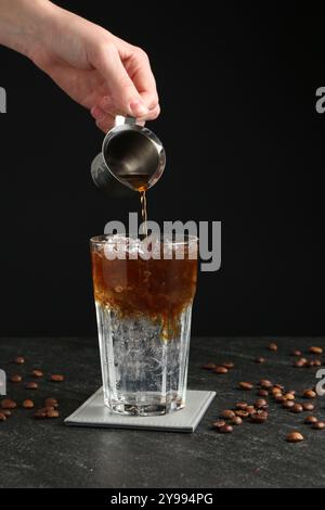 Donna che prepara rinfrescanti bevande toniche per espresso al tavolo buio, primo piano Foto Stock