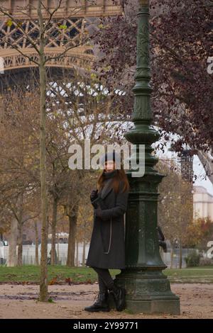 Elegante giovane donna in camice invernale a piedi nel Parco di Parigi vicino alla Torre Eiffel Foto Stock