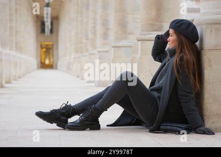 Donna rilassata in stile invernale seduta nel Palais Royal Courtyard di Parigi Foto Stock