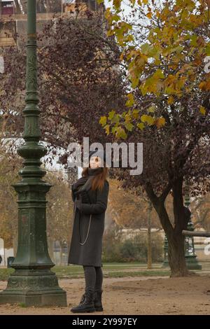 Bella donna parigina che cammina nel parco autunnale con la Torre Eiffel alle sue spalle Foto Stock