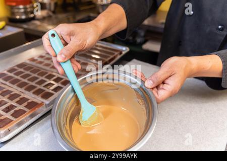 Il cioccolataio mescola il cioccolato al latte fuso con una spatola in un recipiente di metallo in una cucina professionale. Messa a fuoco selettiva Foto Stock