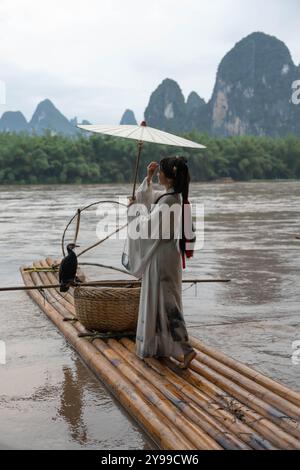 Donna in abbigliamento Hanfu tiene un ombrello mentre si trova su una zattera di bambù a Xingping, Cina Foto Stock