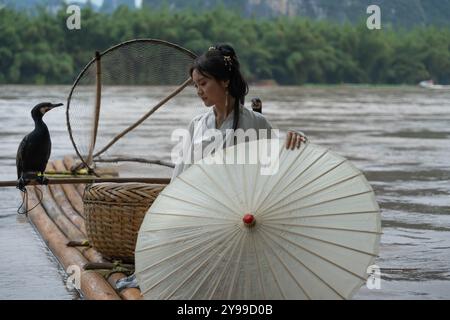 Ragazza della dinastia Han con i capelli lunghi e un ombrello accanto a un cormorano sul fiume li. Xingping, Cina Foto Stock