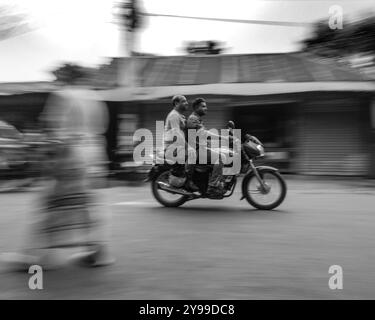 Moto offuscato con due piloti che attraversano una strada trafficata del Bangladesh. Fotografia in bianco e nero con sfocatura in movimento. Foto Stock