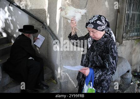 Kapparot, donna che alza un gallo sulla testa, suo marito nella schiena prega poco prima di fare lo stesso, davanti a Yom Kippur o al giorno dell'Atonement. Foto Stock