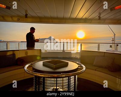 A bordo della nave da crociera Lindblad Nat Geo in Antartide, un passeggero gode dello splendido tramonto sull'Oceano meridionale, con un'isola in vista Foto Stock