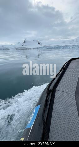 Primo piano di una barca da spedizione che naviga attraverso le calme acque antartiche, con una vista delle montagne innevate e dei ghiacciai in lontananza Foto Stock