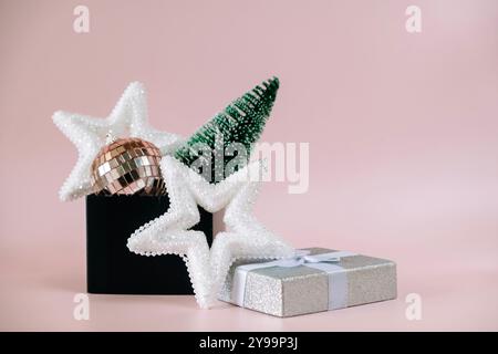 Natale, Capodanno composizione con confezione regalo aperta, piccolo albero di Natale verde e decorazioni su sfondo rosa pallido. Vista frontale Foto Stock