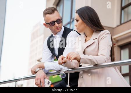 Coppia elegante in un abbigliamento elegante impegnata in una conversazione sul balcone della città. Foto Stock