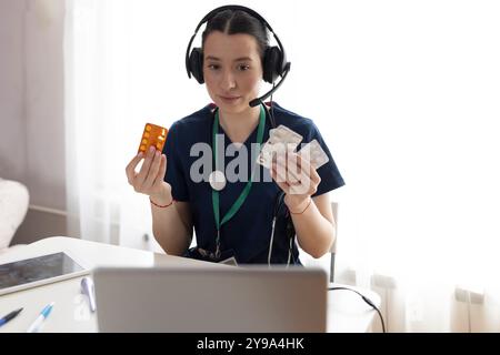 Una donna di medicina generale indossa un cappotto bianco e una cuffia che parla videoconferenza su un computer portatile utilizzando l'app di consultazione per videochiamate online. Foto Stock