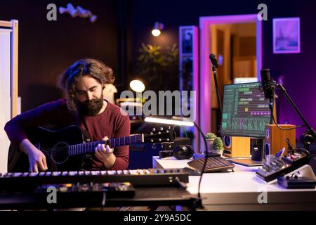 Giovane produttore musicale che suona la chitarra e crea canzoni utilizzando il software daw digitale. Musicista cantante che registra musica in studio domestico, ingegnere audio che mixa brani pop rock utilizzando apparecchiature moderne. Foto Stock