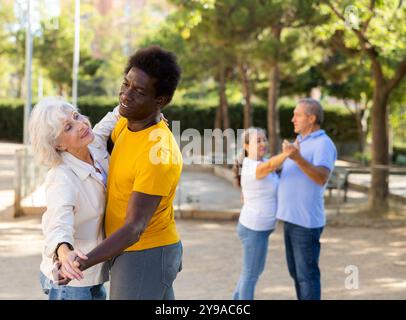 Felici i pensionati multinazionali maturi che trascorrono il tempo insieme e ballano in coppia all'aperto Foto Stock