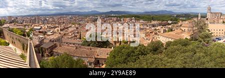 Vista panoramica di Girona, paesaggio urbano e montagne circostanti sotto il cielo nuvoloso, Spagna e Catalogna Foto Stock