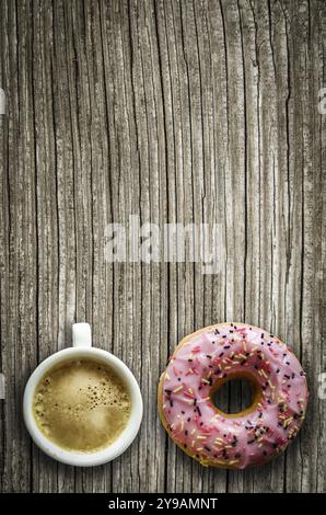 Retrò immagine filtrata di una ciambella di rosa e una tazza di caffè su una tavola in legno rustico con spazio di copia Foto Stock