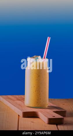 Frullato di frutta sano in un recipiente con paglia e ghiaccio con fondo blu sfumato. Foto Stock