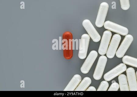 Concetto medico-farmaceutico minimale con pillole bianche sparse su superficie grigia e singola pillola rossa messa a fuoco, simbolicamente rappresentativo unico Foto Stock