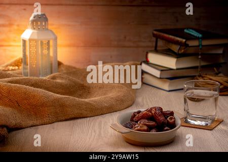Molte palme di datteri sono su ciotole, piatti, una tazza d'acqua, e Corano, una lampada in stile Islami sui tavoli di legno, per aspettare il tempo di Iftar, con il co Foto Stock