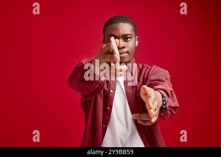 uomo emotivo aspetto africano con telefono nelle mani tecnologia gioia di comunicazione, isolato su sfondo rosso ritratto studio Foto Stock
