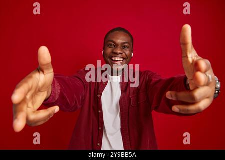 ritratto di un uomo afroamericano emotivo che si rallegra con le mani allungate alla macchina fotografica isolata su sfondo rosso, ritratto in studio Foto Stock