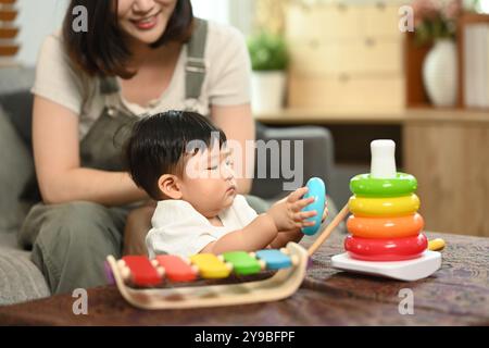 Amata giovane madre e simpatico bambino che gioca con un giocattolo didattico nel soggiorno Foto Stock