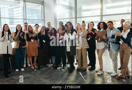Un gruppo eterogeneo di professionisti che applaudono entusiasticamente a una conferenza durante una sessione di formazione aziendale in un ambiente di ufficio moderno. Foto Stock