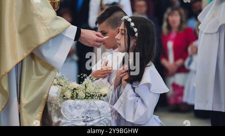 Lida, Bielorussia - 15 giugno 2021: Sacerdote cattolico che amministra la prima Santa comunione ai bambini durante la cerimonia della chiesa Foto Stock