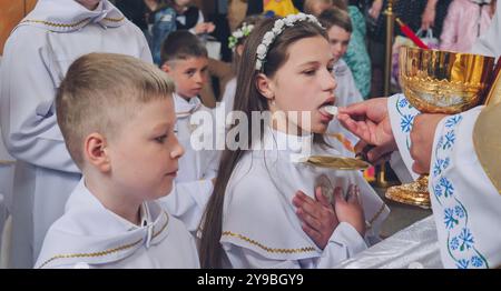 Lida, Bielorussia - 15 giugno 2021: Sacerdote che dà la prima Santa comunione a adolescenti durante la messa Foto Stock