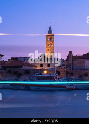 Rab, Croazia - 19 agosto 2023: Una tranquilla città costiera di Rab in Croazia al crepuscolo con un campanile, lungomare, barca della guardia costiera davanti, AN Foto Stock